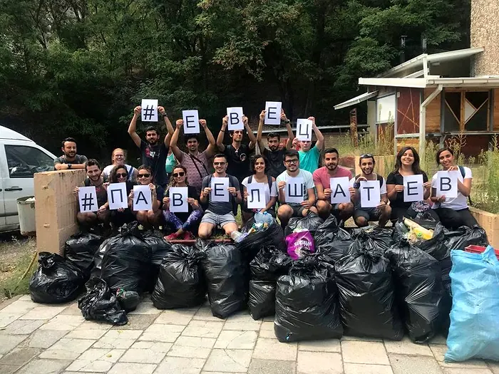 Volunteers in Kocani holding letters spelling EVEC and Pavel Satev behind about twenty bags of waste collected during a clean-up action.