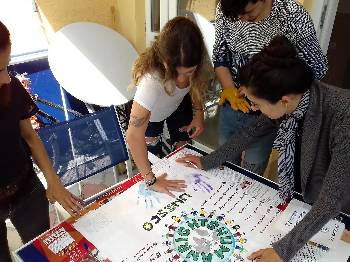 Volunteers pressing painted handprints onto a UNESCO human rights poster at the EVEC Kocani office