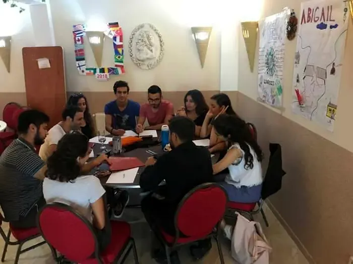 Participants working at tables in the EVEC office, with international flags and project posters on the wall