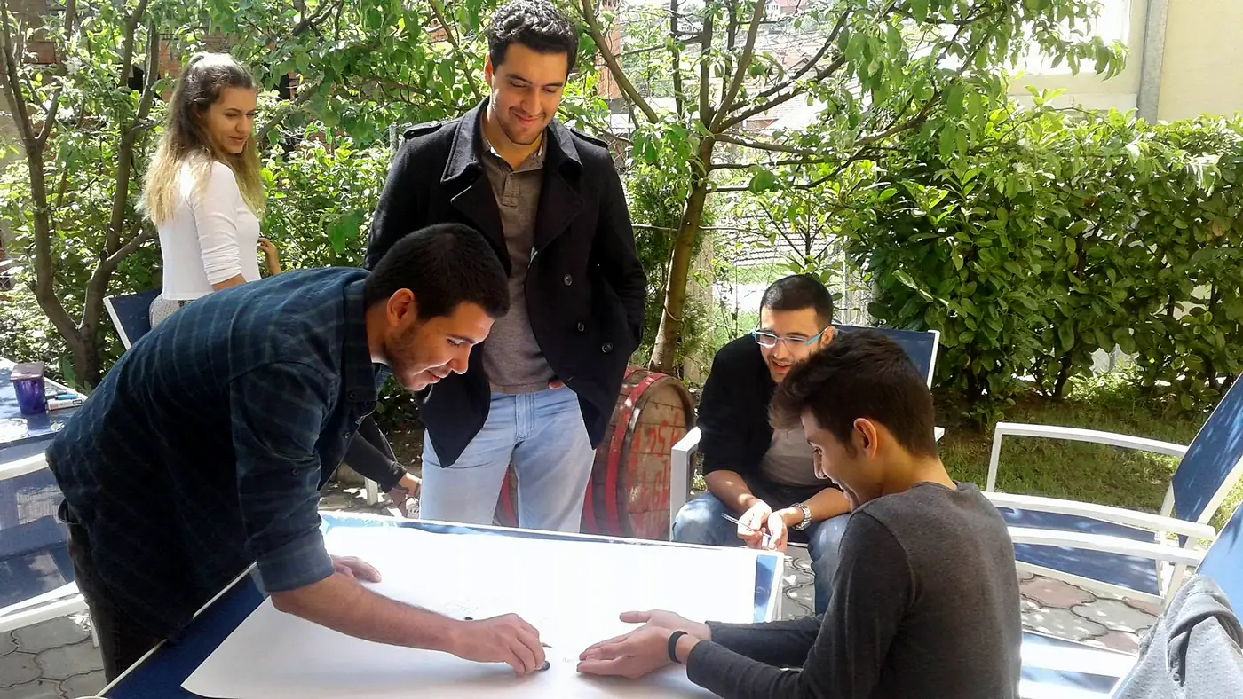 Five EVEC volunteers planning a project on a large sheet of paper at an outdoor table in the garden of the EVEC office in Kocani