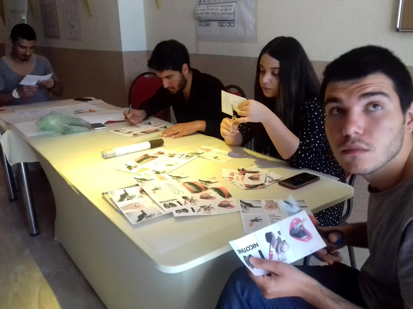Participants with anti-nicotine awareness cards and craft materials at a youth exchange session in Kocani